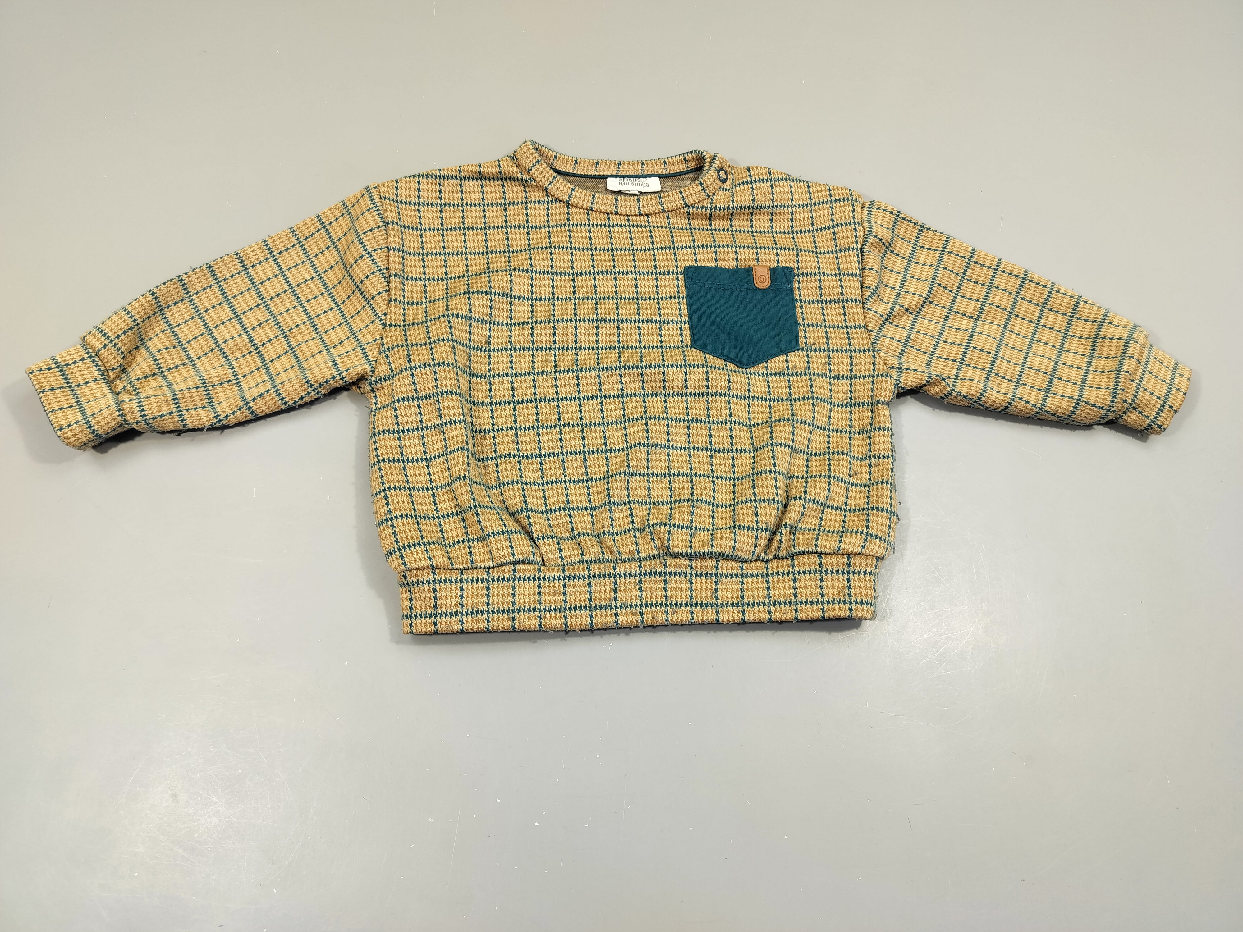 Pull à carreaux bleu et jaune moutarde, poche bleue. Un peu bouloché.