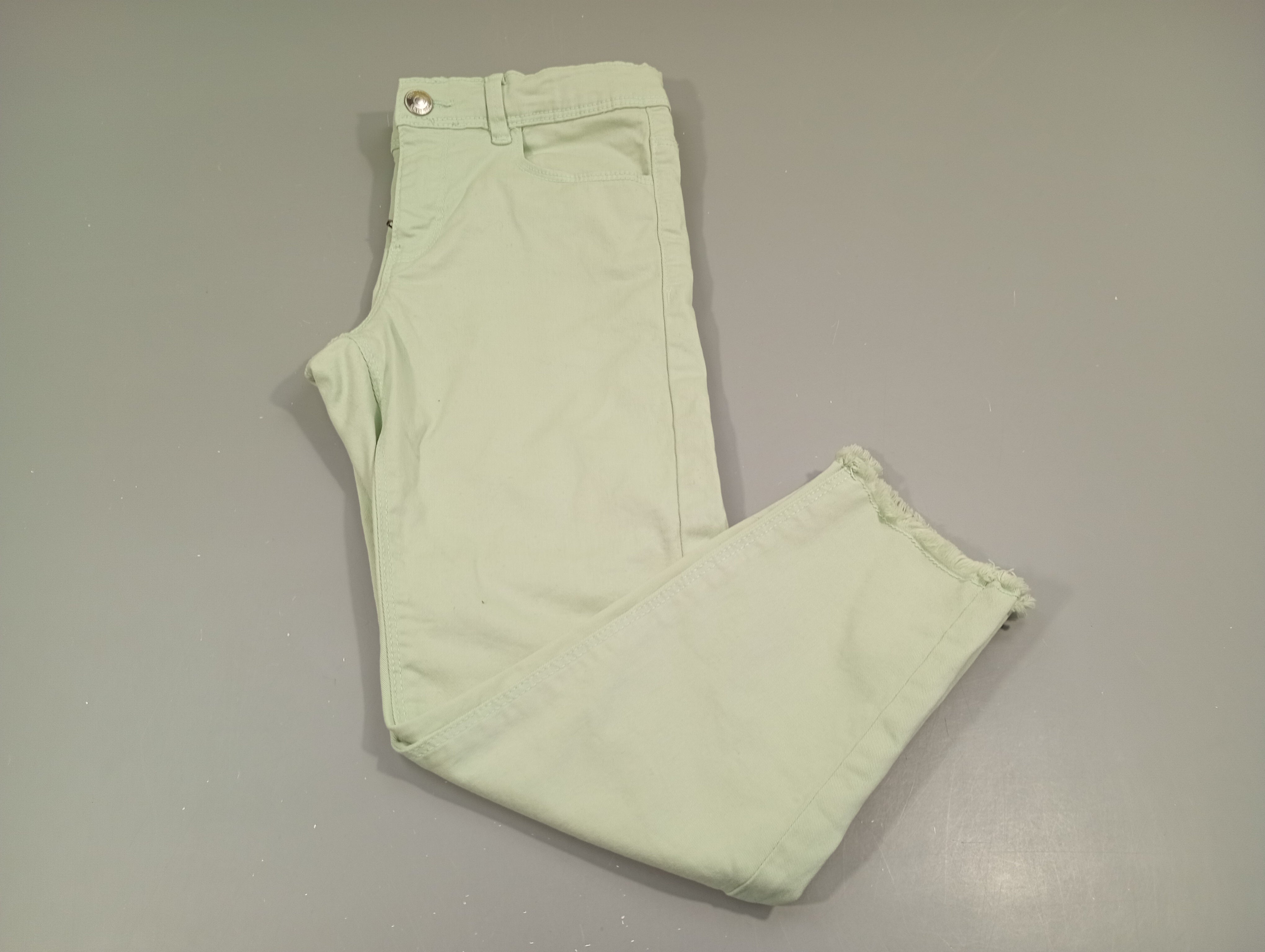 Pantalon denim vert clair, effiloché aux chevilles , petite tache à la jambes gauche