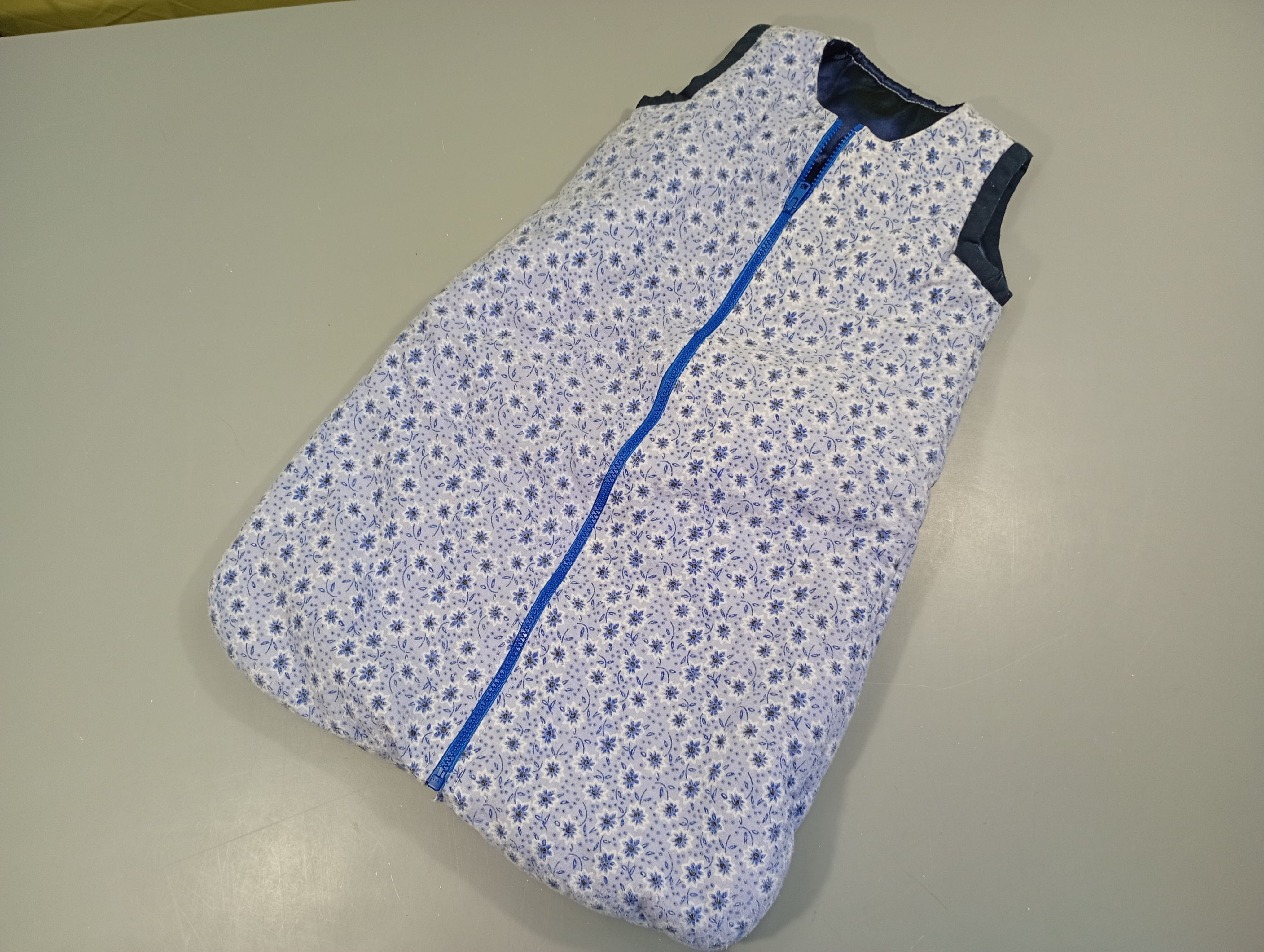 Sac de couchage bleu à fleur, légèrement bouloché. Intérieur noir satiné -65cm