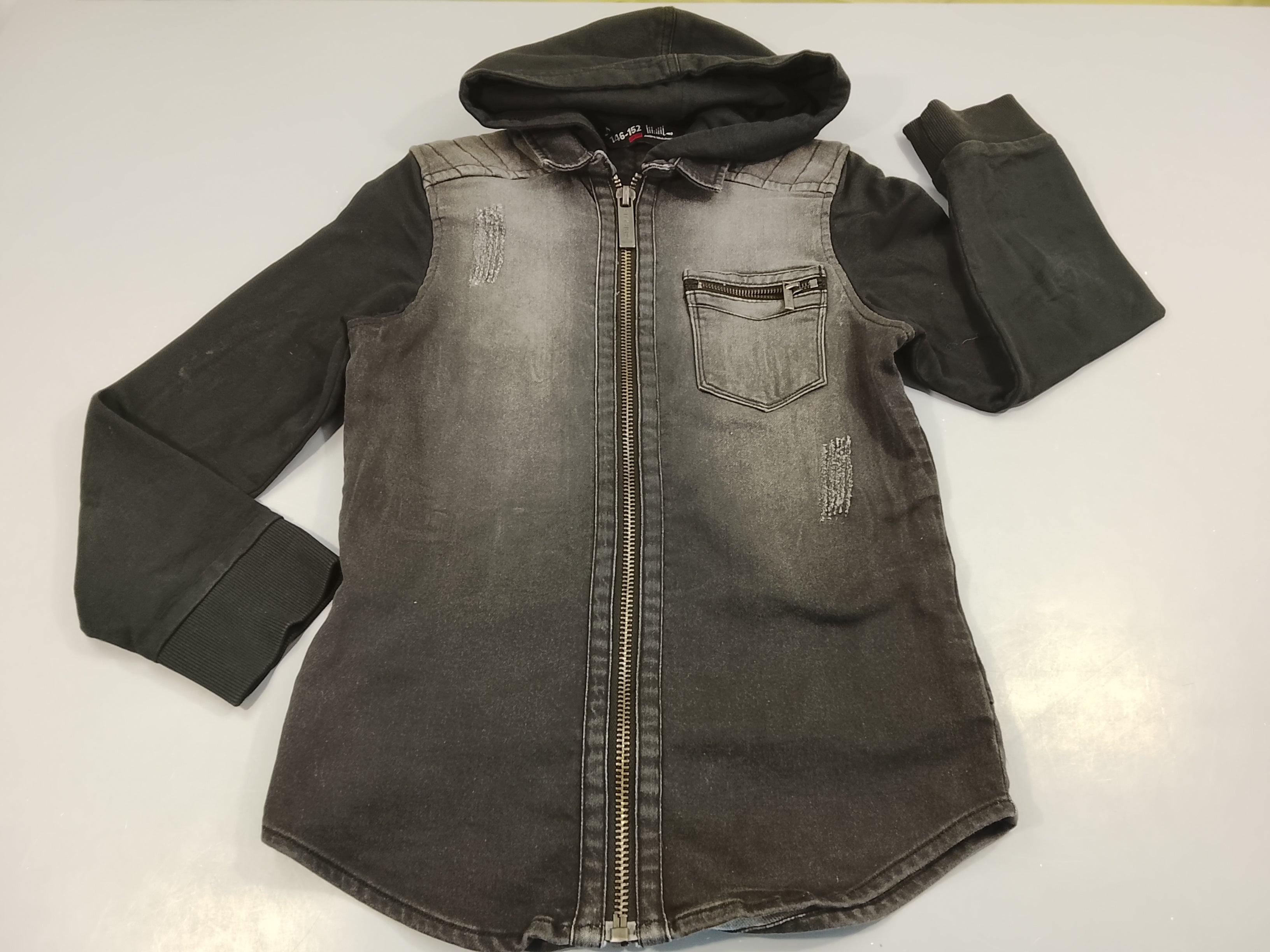 Veste zippée à capuche noir bi-matière, effet éraillé. Tachée à la manche, à relaver