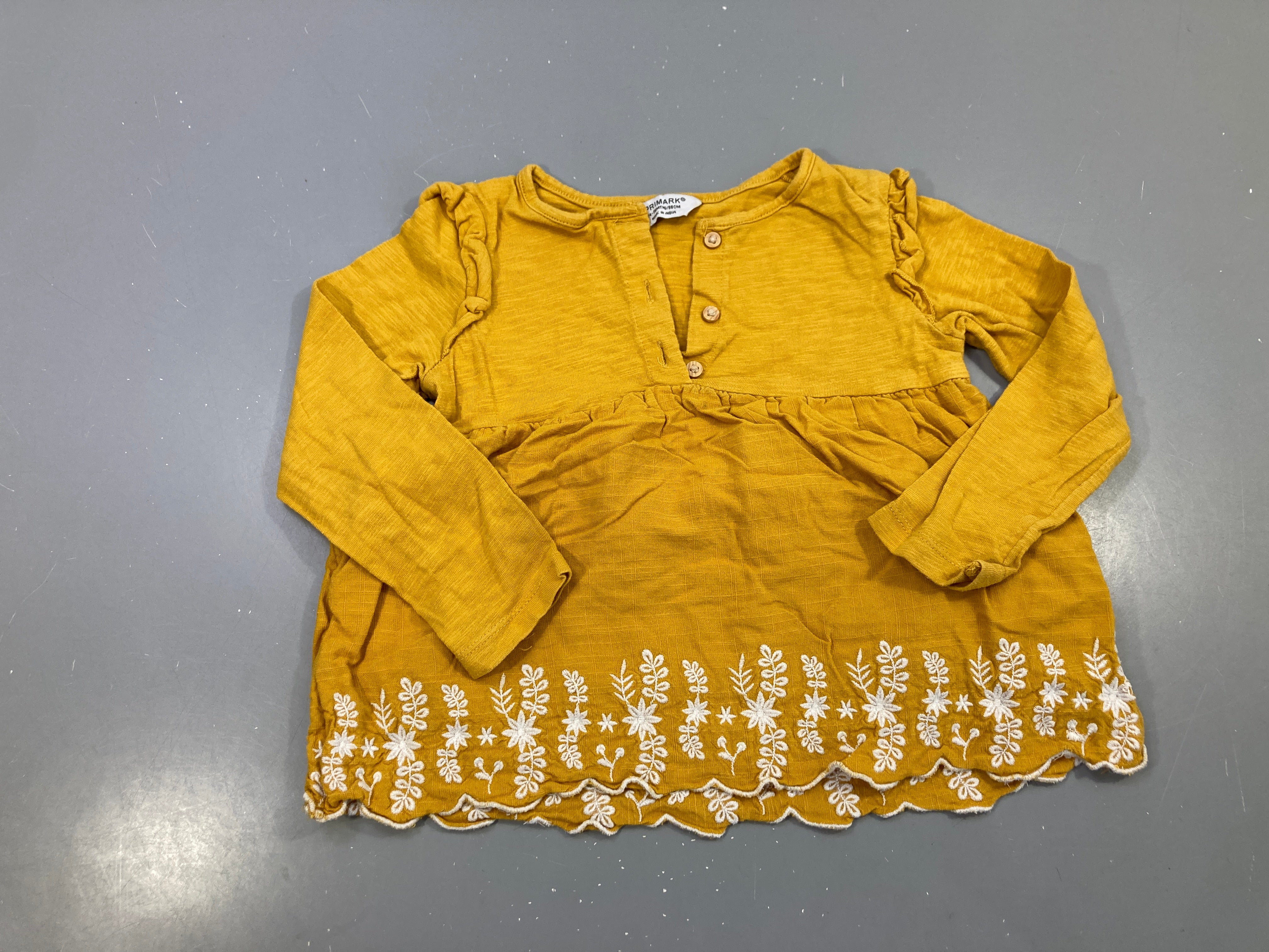 Blouse m.l jaune moutarde boutonnée, volants épaules, bas brodé blanc
