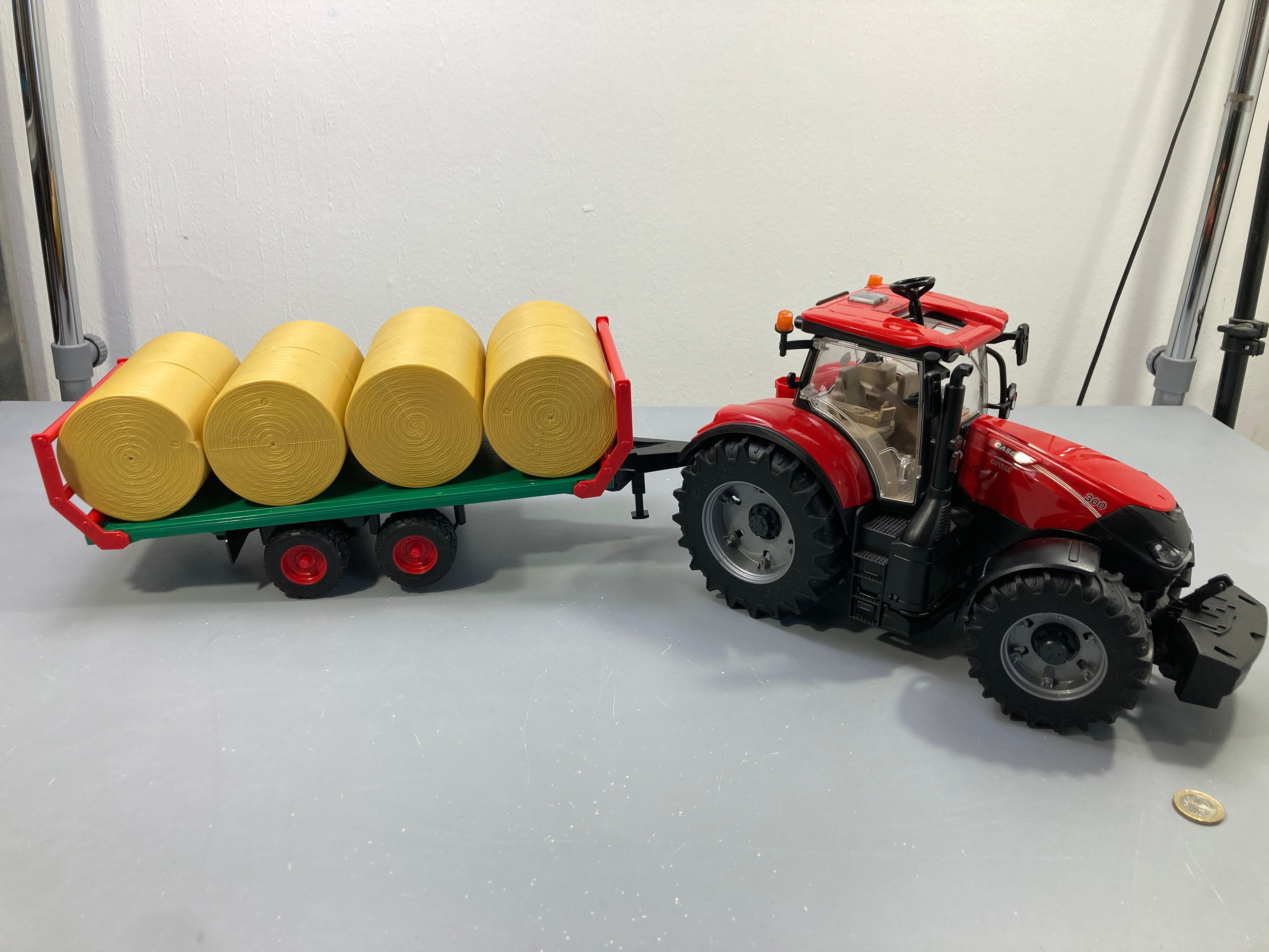 Tracteur rouge Case IH Optum 300 avec remorque plateau verte et 4 balles de foin rondes, Bruder